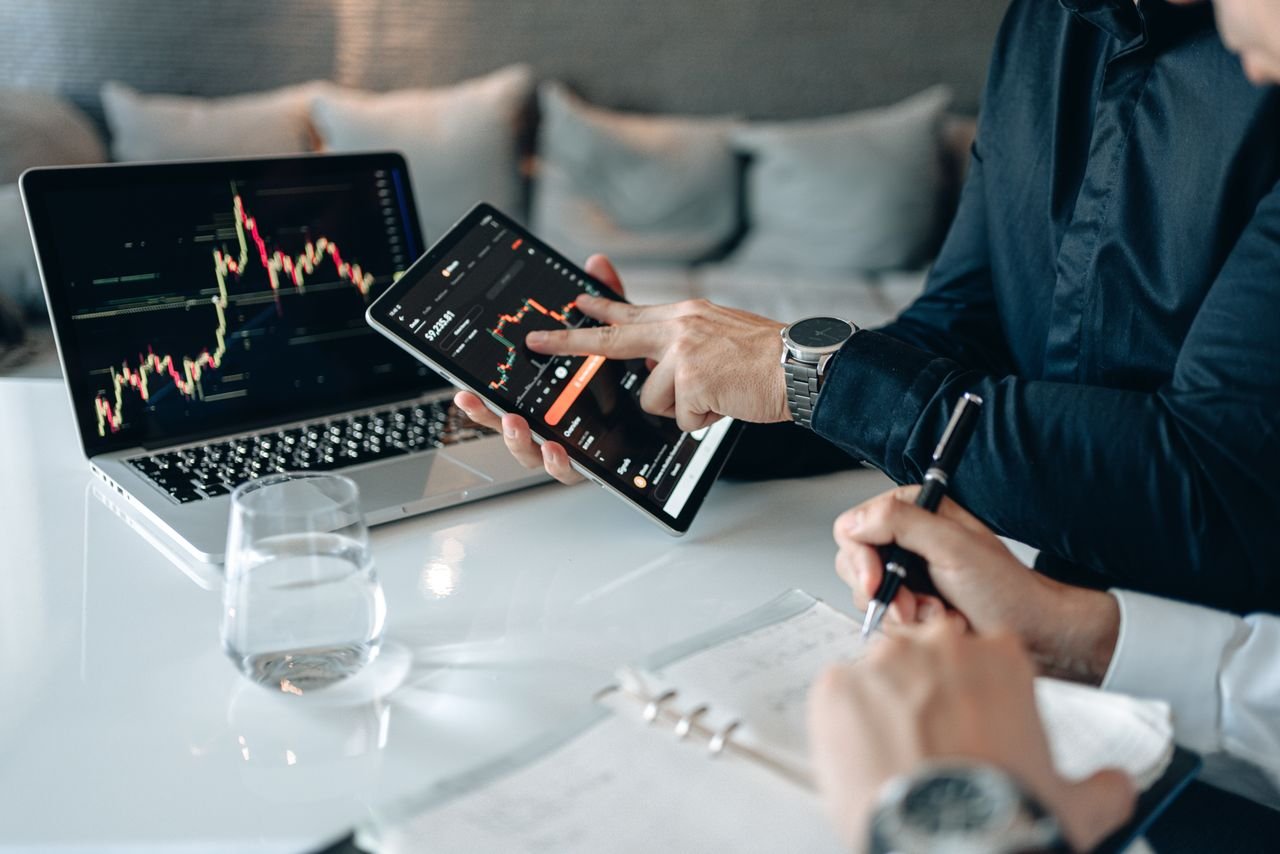 Professionals analyzing financial data on a tablet and laptop in an office setting.